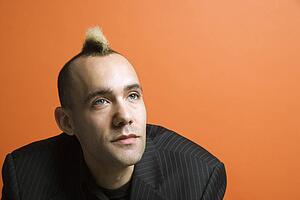 Caucasian man in suit with mohawk against orange background.