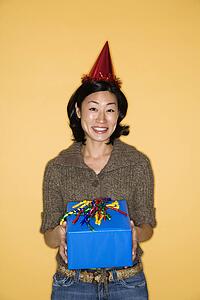 Pretty mid adult Asian woman wearing party hat holding present.