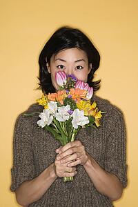 Pretty mid adult Asian woman holding bouquet of flowers up to face.