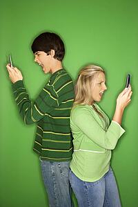 Boy and girl on cellphones standing with backs to each other
