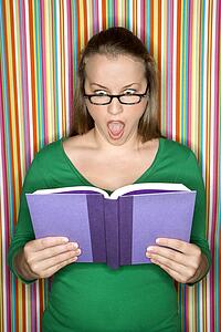 Young Caucasian female adult reading book making expression.