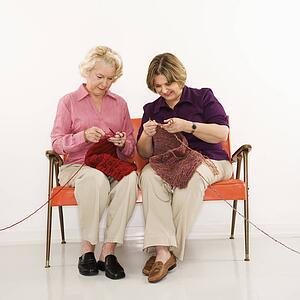 Caucasian middle aged woman and senior woman sitting and knitting.
