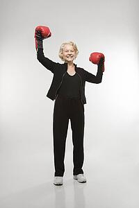 Caucasian senior woman wearing boxing gloves raised in the air.