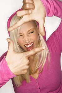 Portrait of attractive blonde Caucasian young adult woman wearing fuchsia holding hands up to make frame around face.