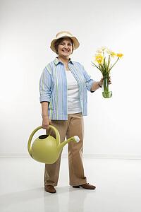 Caucasian middle aged woman holding flowers and watering can.