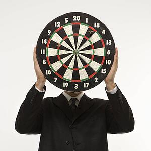 Man wearing suit and holding dartboard in front of face.