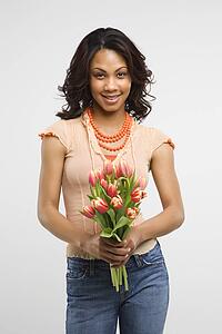 Studio shot of stylish woman holding bouquet of tulips smiling and looking at viewer. 