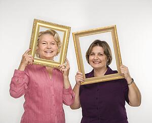 Mature woman and senior woman holding picture frames over faces