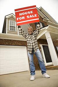 Male outside house holding up for sale sign