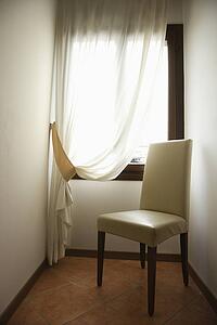 Empty chair by window with drapes in Venice, Italy.