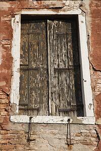 Worn building with window with closed wooden shutters in Venice, Italy.