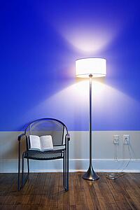Blue projection light on wall with bright floor lamp and open book on chair