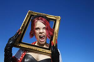 Young adult Caucasian female holding empty frame around head.