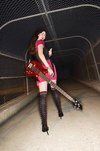 Caucasian young adult female walking with electric guitar in skywalk looking at viewer and gesturing.