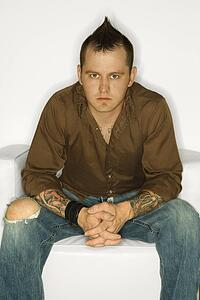 Man with mohawk sitting with hands clasped together