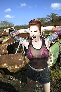 Sexy tattooed woman yelling and holding her hands over her ears in junkyard
