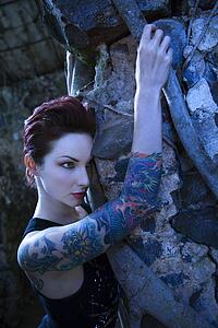 Blue-toned portrait of fearful looking tattooed woman next to concrete wall 
