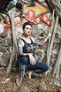 Sexy tattooed woman crouching next to wall covered in graffiti and Banyan tree branches