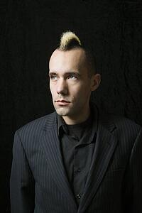 Portrait of Caucasian man in suit with mohawk against black background.