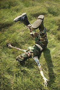 Attractive tattooed Caucasian woman in camouflage lying on grass with her legs up in the air 