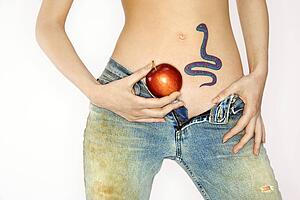 Portrait of attractive young woman holding apple by snake tattoo on stomach