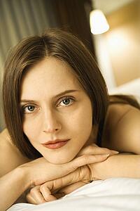 Portrait of Caucasian mid-adult woman looking at viewer with head resting on hands.