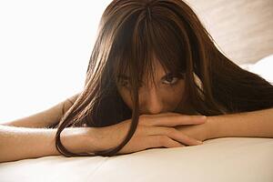 Pretty young Caucasian woman lying on bed making eye contact.