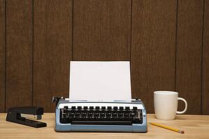 Vintage typewriter, coffee cup, pencil and stapler on desk.