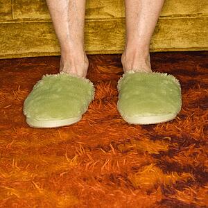 Caucasian senior female feet wearing green bedroom slippers on carpet.