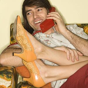 Mid-adult man talking on telephone with mid-adult woman's legs draped over lap