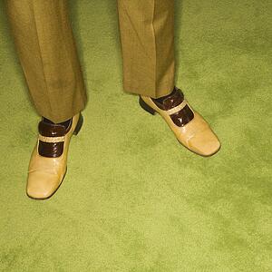 Close-up of male feet in vintage shoes against green rug.