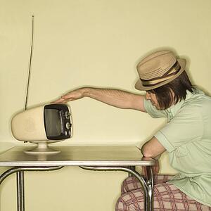 Man wearing hat sitting at 50's retro dinette set tapping old television set