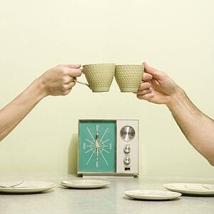Caucasian male and female hands toasting with coffee cups across retro kitchen table setting.