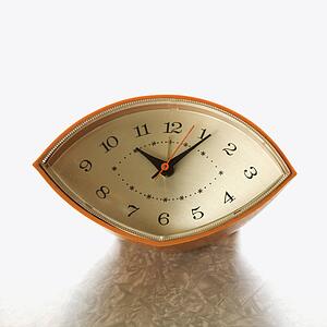 Still life of orange eye-shaped vintage clock on table.