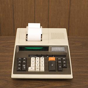 Still life shot of a vintage calculator sitting on a wooden desk