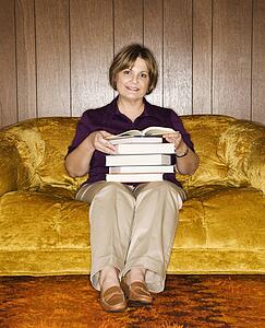 Woman sitting on couch in living room holding stack of books.