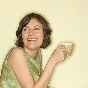 Pretty mid-adult woman holding up coffee cup and smiling