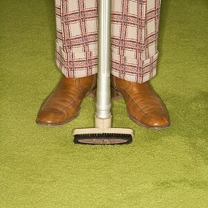 Close-up of male legs in plaid pants with vacuum extension standing on green retro carpet