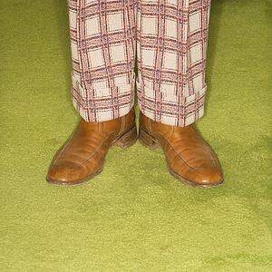 Close-up of Caucasian male legs in plaid pants standing on green retro carpet.