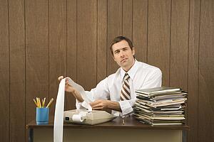 Mid-adult Caucasian male holding printout from calculator in office setting.