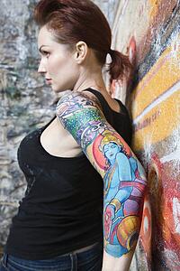 Sexy tattooed woman leaning on wall covered in graffiti