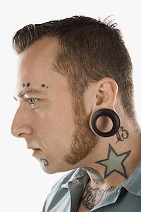 Caucasian mid-adult man with tattoos and piercings.