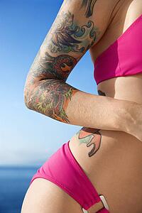 Tattooed woman in hot pink bikini with Pacific Ocean in background 
