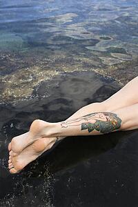 Legs of tattooed woman lying in tidal pool 