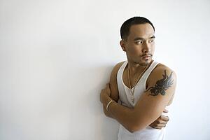 Portrait of young adult man leaning against white wall with arms crossed looking over shoulder