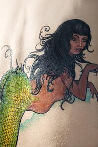 Close-up of Caucasian woman's back with mermaid tattoo.