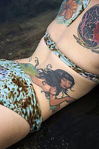 Sexy tattooed Caucasian woman in bikini lying in tidal pool 