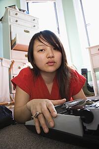 Pretty Asian young woman lying on floor in red robe typing on typewriter.