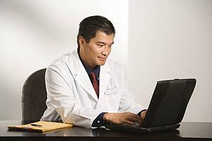 Man in a lab coat typing on a laptop computer at a desk