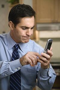 MId-adult Caucasian male pressing cell phone buttons while standing in kitchen.